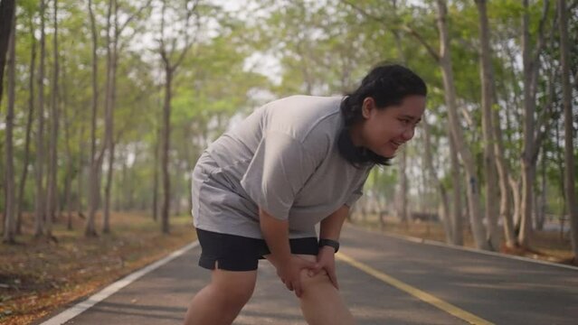 An overweight woman gets painful muscle cramp while doing  her morning exercise run at a public park