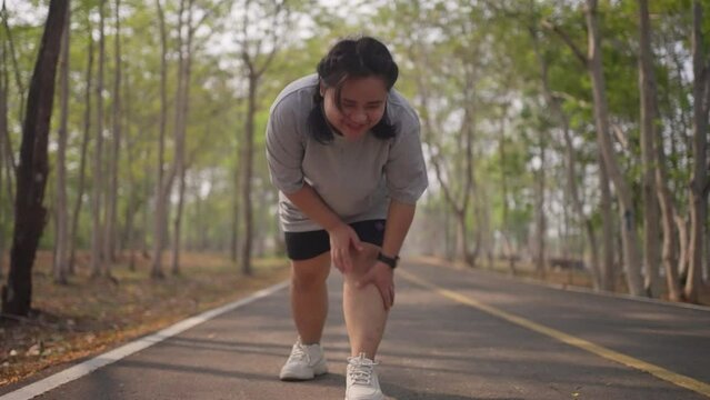 An overweight woman gets painful muscle cramp while doing  her morning exercise run at a public park