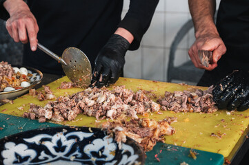 male chefs cut boiled beef meat with knives on a cutting board for cooking oriental Uzbek pilaf in...
