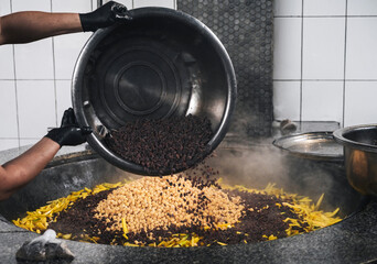 male chef's hands add raisins to a cauldron with chickpeas and yellow carrots to cook Uzbek pilaf...
