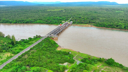 The colossal dam looms over the churning river, its floodgates standing sentinel against nature's...