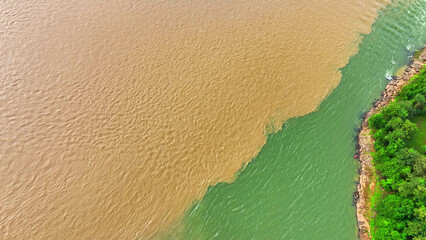 From above, two rivers meet, one adorned in vibrant orange, the other in lush emerald green,...
