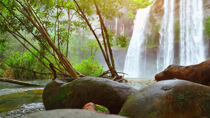 Mesmerizing waterfall cascades from towering cliff amid vibrant tropical greenery, nature's grand...