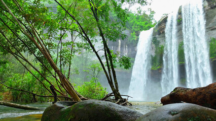 Majestic waterfall cascades from towering cliff in lush tropical jungle, a breathtaking sight. Huai...