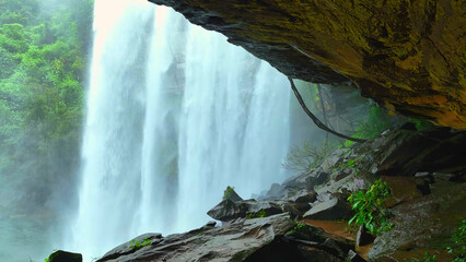 Glistening waterfall seen through cave's embrace in lush tropical paradise, nature's hidden gem. Huai Luang Waterfall, Phu Chong Na Yoi national park, Ubon Ratchathani Province, Thailand. 
