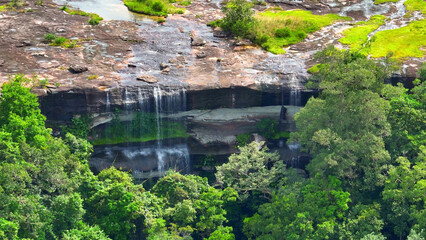 A breathtaking waterfall cascades from a towering cliff, enveloped by vibrant, emerald-hued tropical foliage. Nature's masterpiece. Pha Taem National Park, Ubon Ratchathani Province, Thailand.
