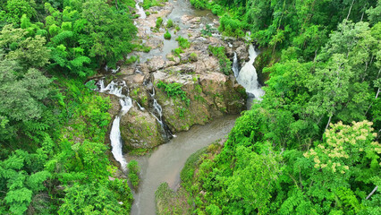 Drone's eye view of a majestic waterfall, embraced by a thriving, green tropical forest. A...
