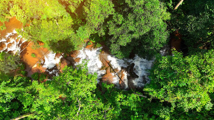 A hidden gem in the lush tropical rainforest, a mesmerizing waterfall glistens through dense emerald foliage, gracefully cascading down rocky tiers. Captured by drone, it's nature's masterpiece.
