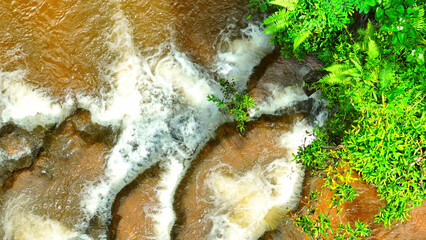 A lush tropical rainforest conceals a stunning hidden waterfall. The emerald cascade flows gracefully over layered rocks, a secret paradise captured from above by drone. jungle paradise. Thailand.