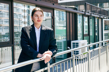A business woman in a jacket stands against the backdrop of a business center6