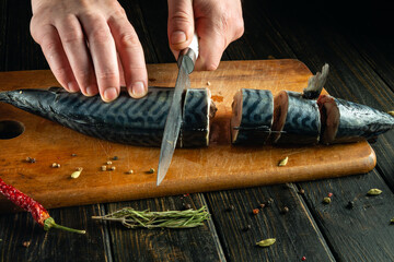 Slicing fish before cooking with a knife in the hands of a chef. The cook cuts mackerel on a...