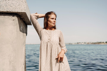 A woman is standing on a dock by the water, wearing a dress and a pair of black shoes. She is smiling and she is happy.