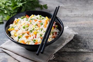 White rice with vegetables in a black bowl on wooden table. Copy space