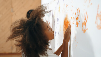 African girl paint the wall with colorful stained hands with friend. Group of multicultural learner...