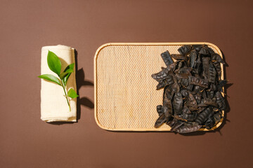 Flat lay of many black locust fruits placed on a bamboo tray. A folded towel with green leaves...