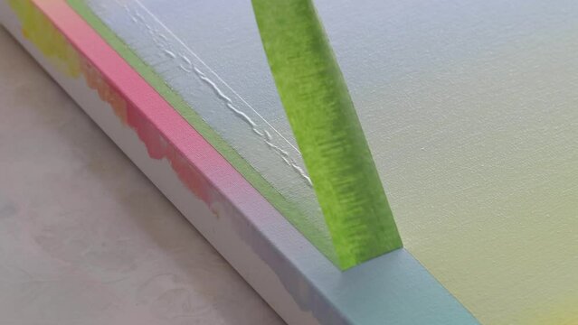 An artist pulls masking tape, to reveal a crisp hard edge gradient painted artist canvas.