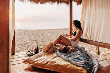 Mature woman looking at sea while sitting in hut holding book on vacation at beach