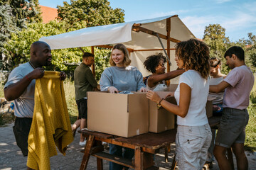 Smiling group of multiracial volunteers helping each other while sorting out clothes during charity drive at community c