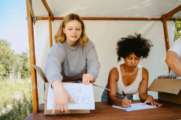 Volunteer helping female colleague while labeling boxes on table during charity program at community center