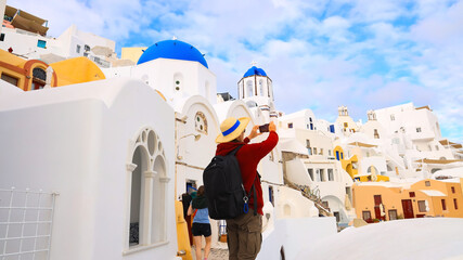 Back view of young tourist man  using smartphone take picture at View of blue church dome in Oia village,Santorini,Greece