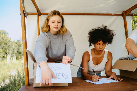 Volunteer helping female colleague while labeling boxes on table during charity program at community center