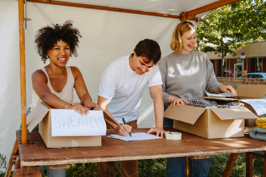 Portrait of happy female volunteers labeling boxes with colleagues while working during charity drive at community cente