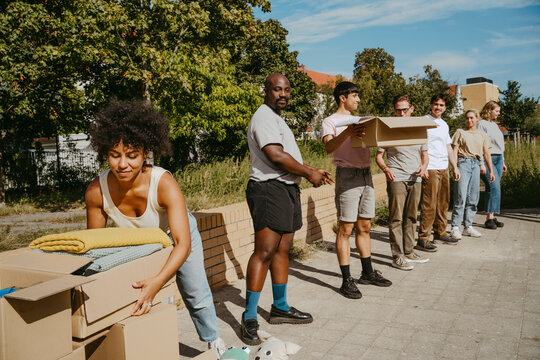 Young female volunteer passing donation boxes to colleagues standing in rows during charity drive at community center