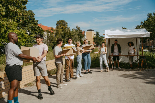 Group of male and female volunteers passing donation boxes while standing in row during charity drive at community cente