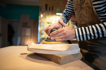 Closeup of sanding wood with orbital sander at workshop, soft focus. Man carpenter polishes wooden...