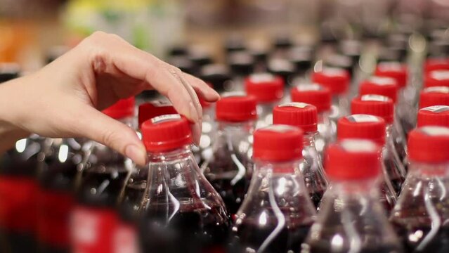 at Supermarket - Many Plastic Bottles with Drinks in Row and Woman Hand Customer Takes one. Caucasian female buyer choosing carbonated drink in store. Close-up footage