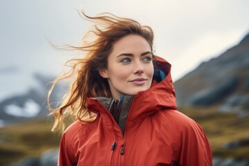 Portrait of a content woman in her 20s wearing a windproof softshell over snowy mountain range
