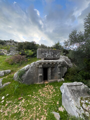 An ancient rock tomb in Xanthos, Kaş, Antalya, Turkey, showcases remarkable architecture and historical significance within a lush and rugged landscape.