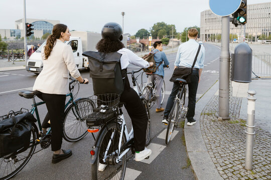 Male and female business professionals waiting at stoplight with bicycles at street in city