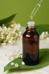 Small brown bottle with dropper and Lily-of-the-valley flowers. Side view. Space for text.