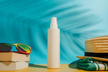 Blank white sunscreen bottle sun hat sunglasses and books on beach in direct sunlight. Summer skin...