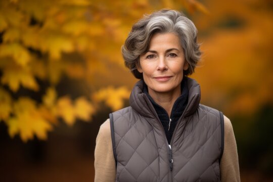 Portrait of a content woman in her 60s dressed in a thermal insulation vest over background of autumn leaves