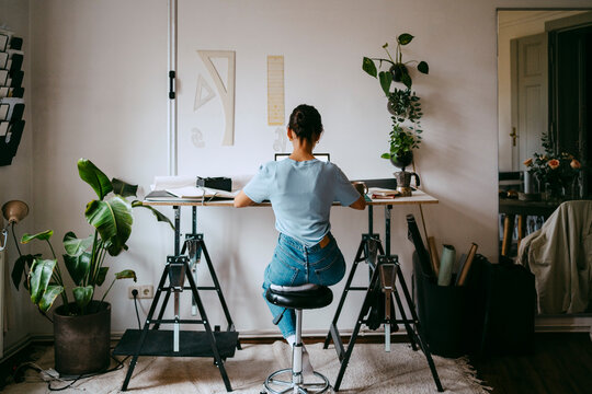 Rear view of female freelancer sitting on stool and working from home