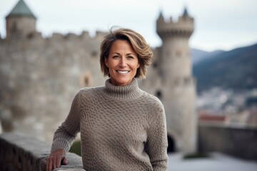 Portrait of a satisfied woman in her 50s showing off a thermal merino wool top isolated on historic castle backdrop