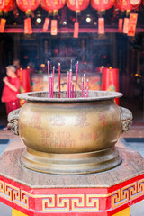 A large brass incense burner with burning sticks releases smoke in a Chinese temple at Jakarta’s Chinatown, surrounded by lanterns and traditional decorations, symbolizing prayers and blessings.