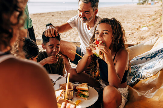 Girl eating sandwich sitting with family in beach hut on vacation