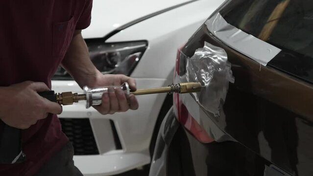 Mechanic skillfully using an electric dent puller on the rear door of a car.