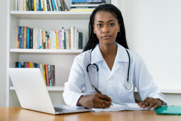 Serious young latin american female doctor writing notes