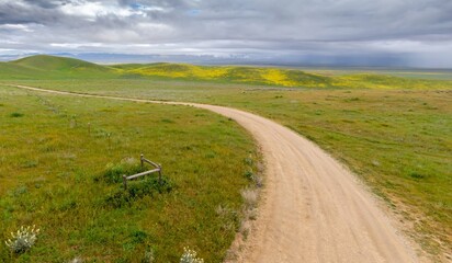 Dirt country road on a ranch and hills during the superbloom in Carrizo National Monument, Santa Margarita, California, United States of America.
