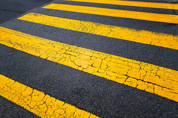 Diagonal lines of an old zebra crossing on a main street in San Francisco, California (USA). Cracked asphalt and weathered yellow paint peeling off the road. Bad driving conditions and need for repair