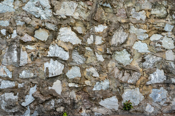 A rough stone wall made of large gray pieces of stone filled with cement mortar.