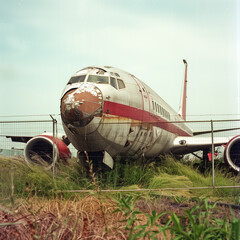 Decommissioned airplane resting in overgrown field behind fence.