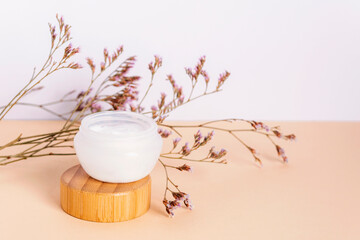 Cosmetic cream in a jar and purple kermek flowers on beige table. Natural cosmetics concept. Closeup