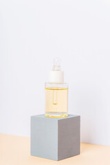 Glass cosmetic bottle with oil or serum on gray podium on beige table. Closeup