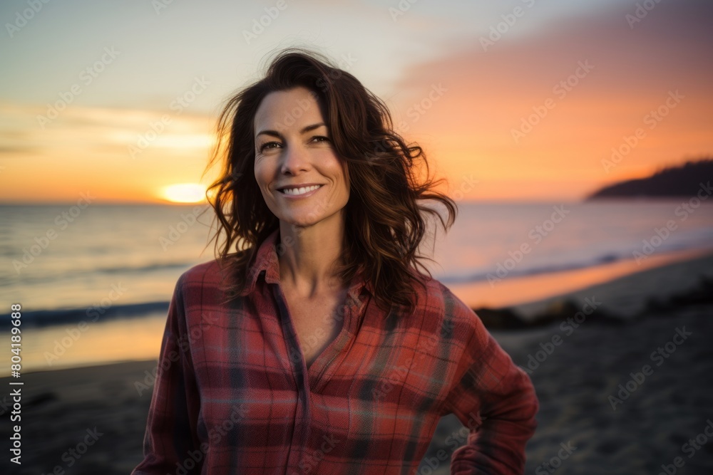 Sticker Portrait of a grinning woman in her 40s dressed in a relaxed flannel shirt in front of beautiful beach sunset