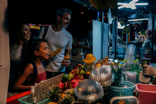 Smiling tourists buying fruit juice from stall at food market on vacation